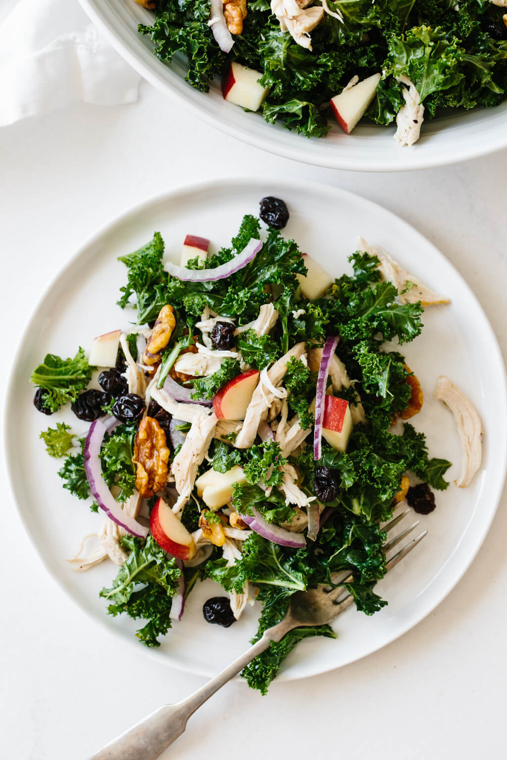 Kale salad with apples and chicken is bursting with autumn flavors in every single bite! An individual plate of kale salad next to a big serving bowl.