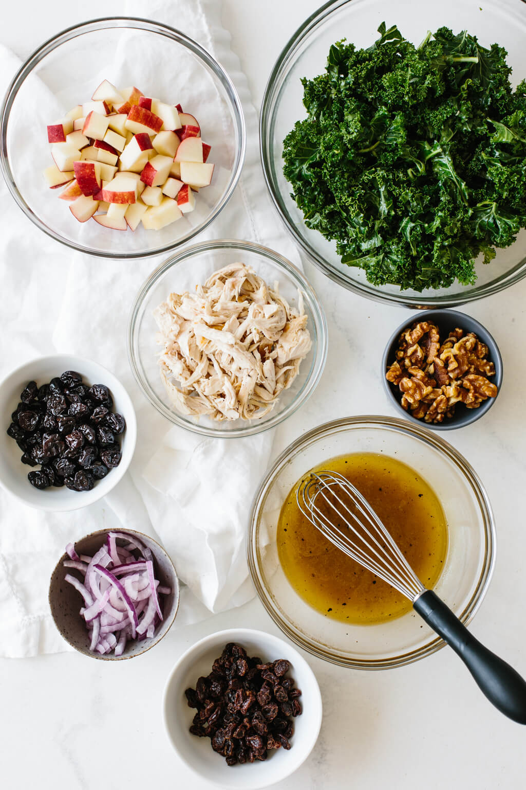 Kale salad with apples and chicken is bursting with autumn flavors in every single bite! Ingredients for the kale salad recipe in individual bowls on a table.