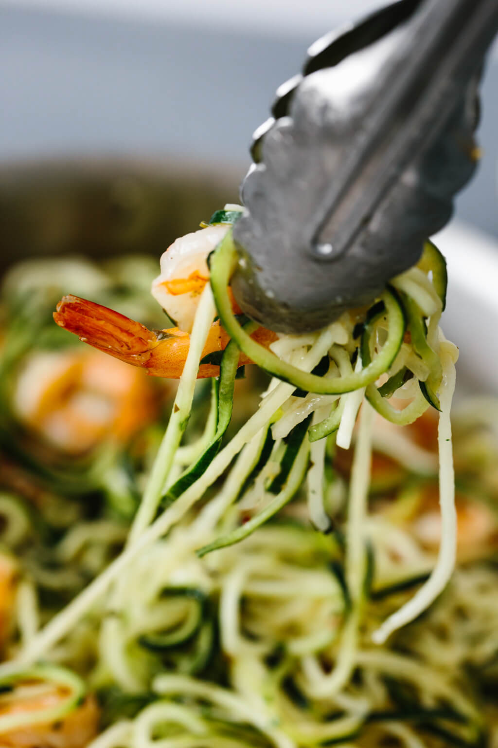 Zucchini noodles pulled out of pan with tongs.