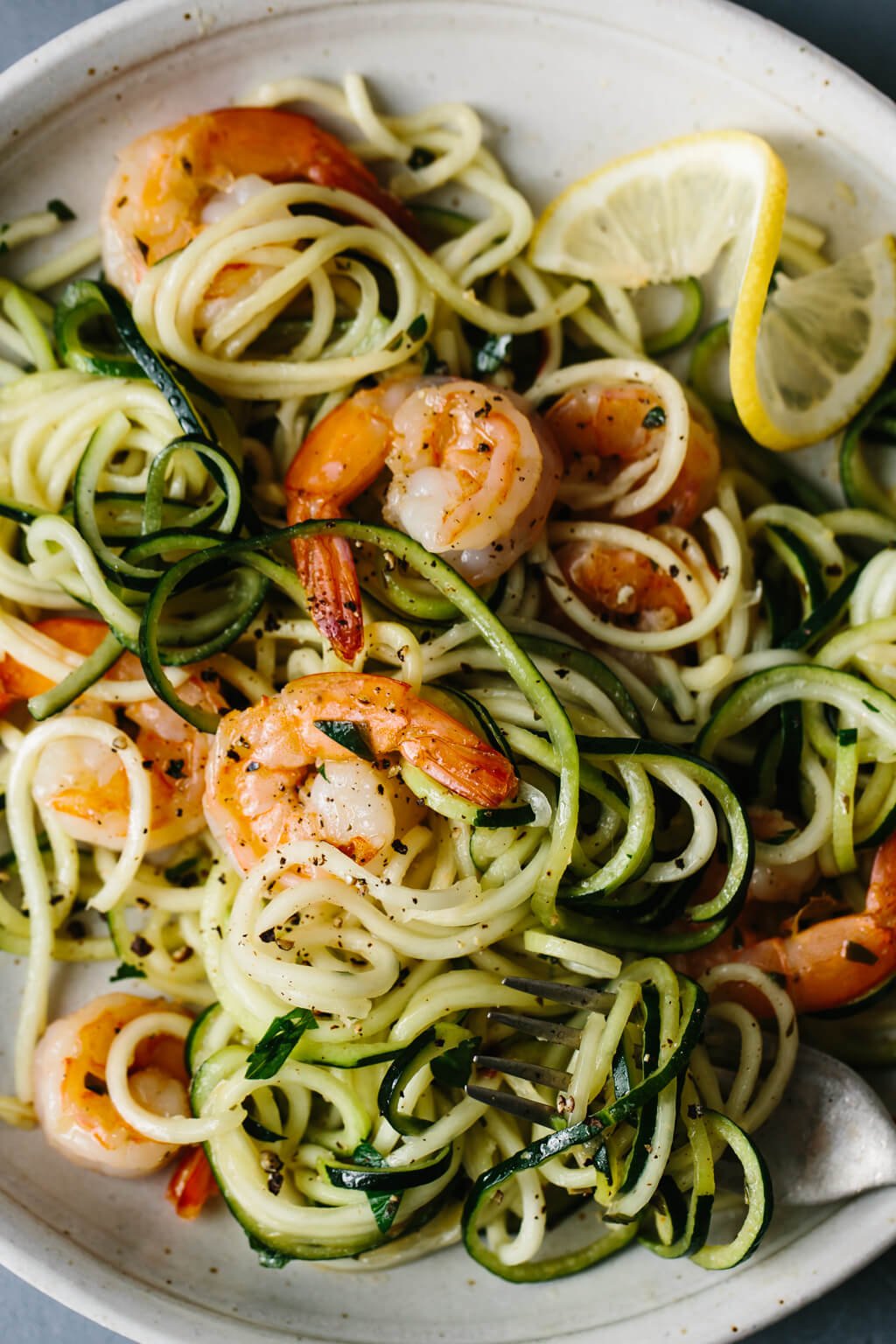 Zucchini noodles pasta and lemon garlic shrimp on a plate next to a slice of lemon.