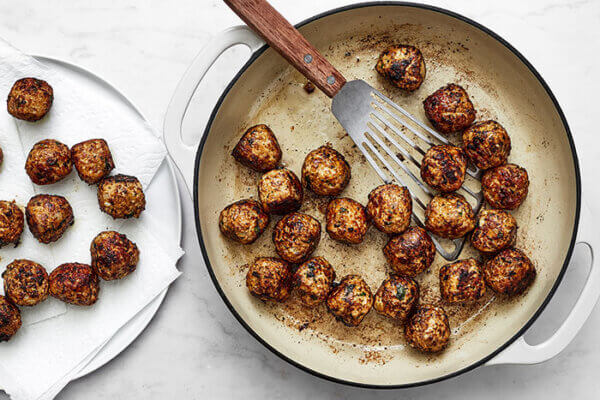 Cooked fennel pork meatballs in a pan with a spatula