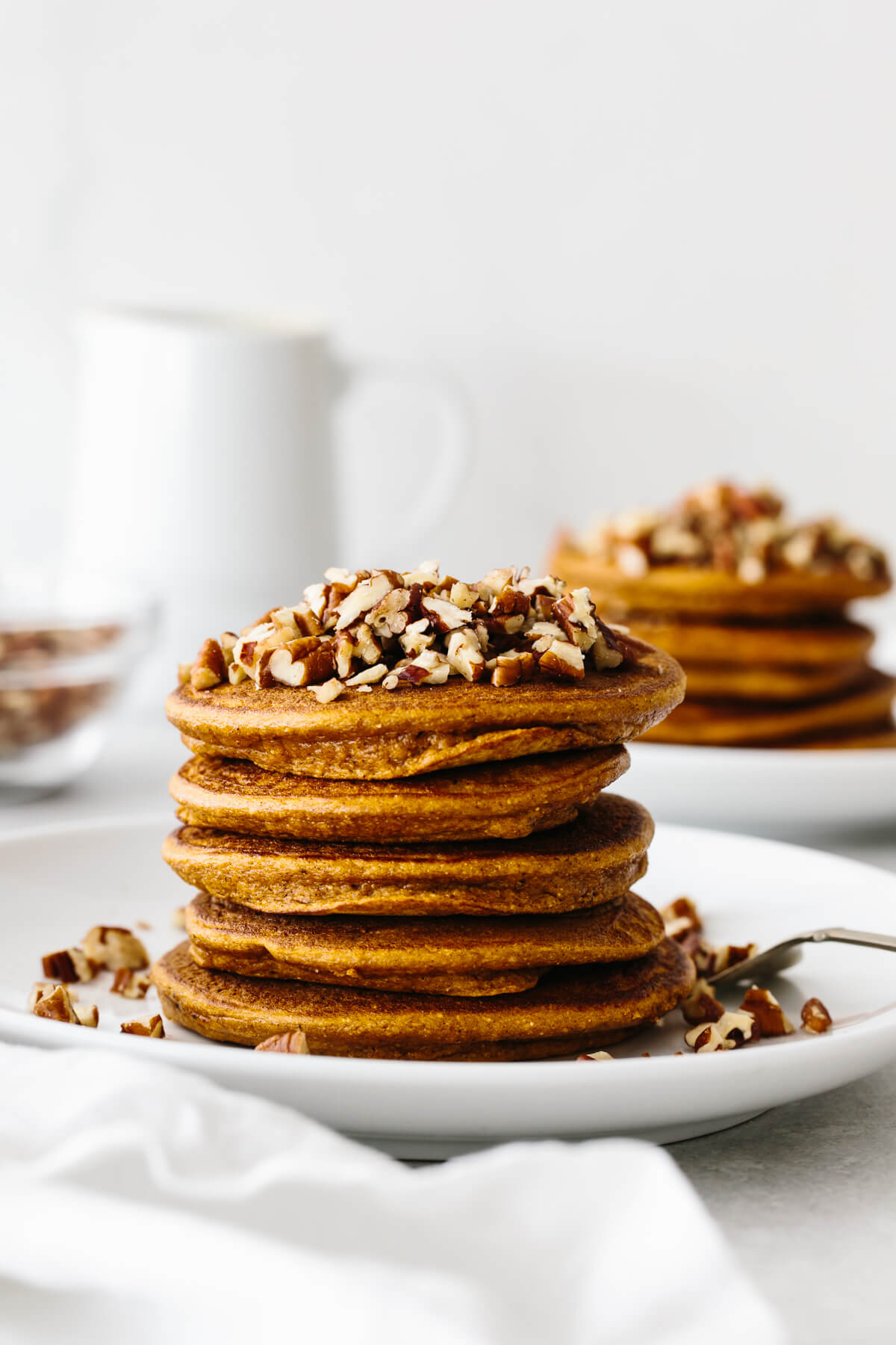 A stack of paleo pumpkin pancakes on a plate, topped with chopped pecans.