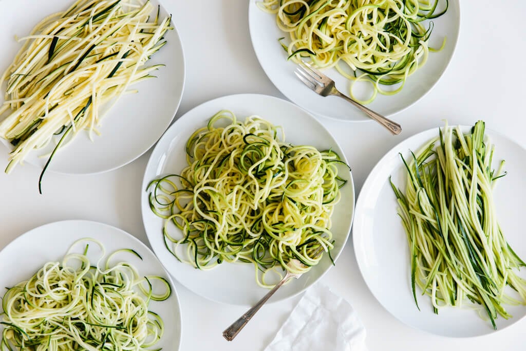 Five plates of zucchini noodles made different ways.