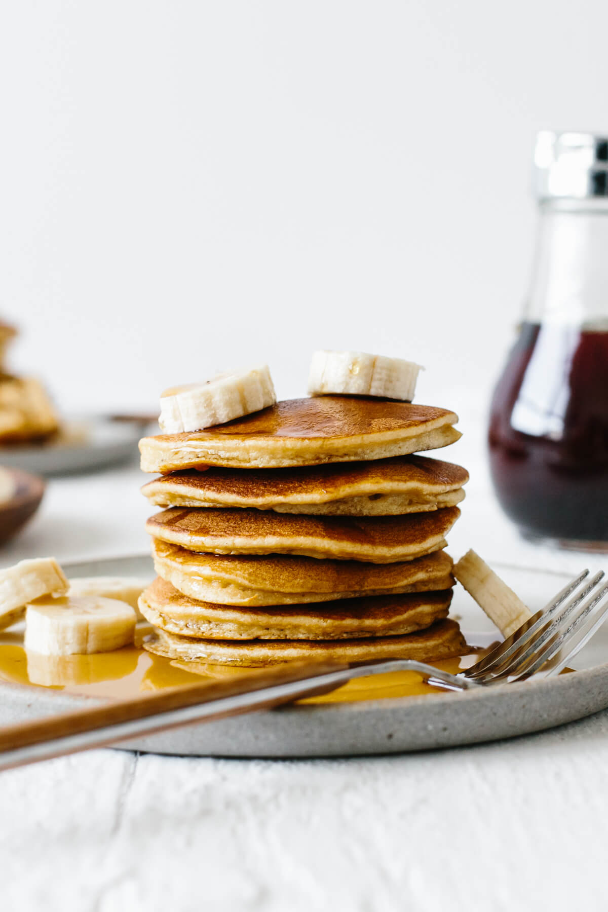 Stack of paleo pancakes on a plate with sliced bananas and syrup.