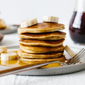 Stack of paleo pancakes on a plate with bananas and syrup.