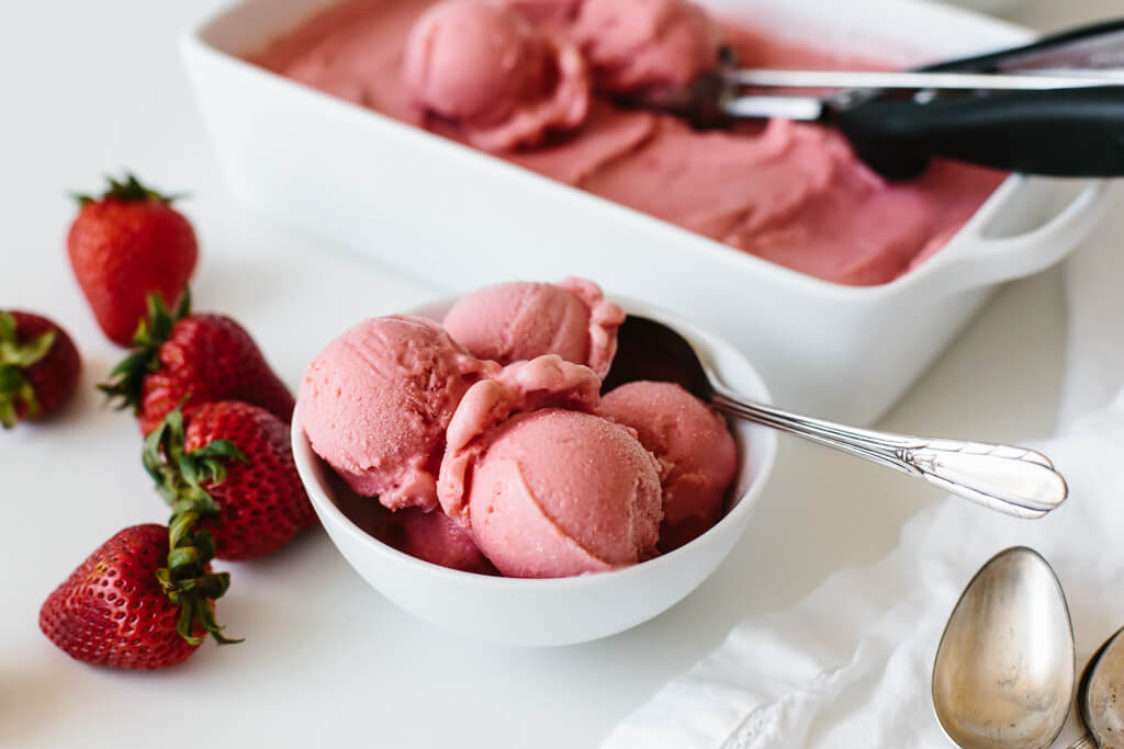 This strawberry frozen yogurt recipe is beyond easy. It takes just three ingredients and 30 seconds! Strawberry frozen yogurt scooped into a white bowl with fresh strawberries next to it.