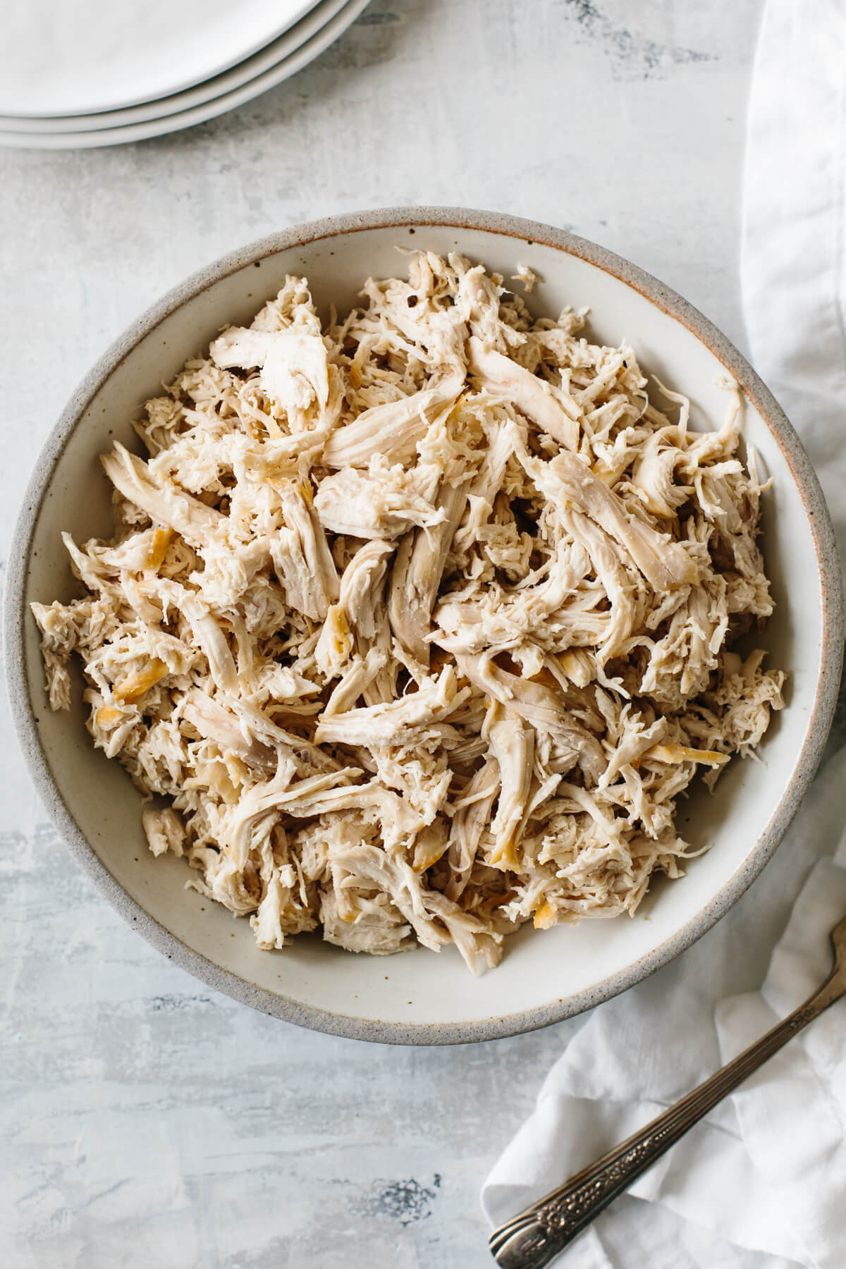Shredded chicken in a bowl next to plates and a napkin.