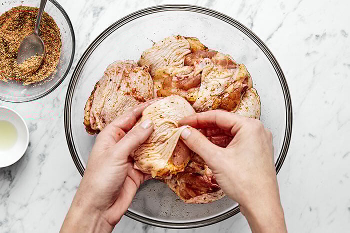 Seasoning chicken with hands.