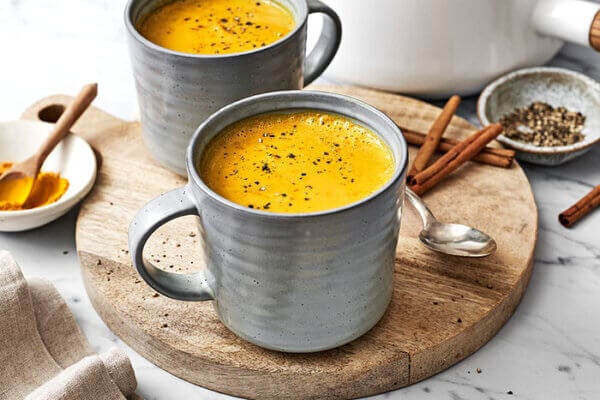 Mugs of turmeric golden milk on a wooden board