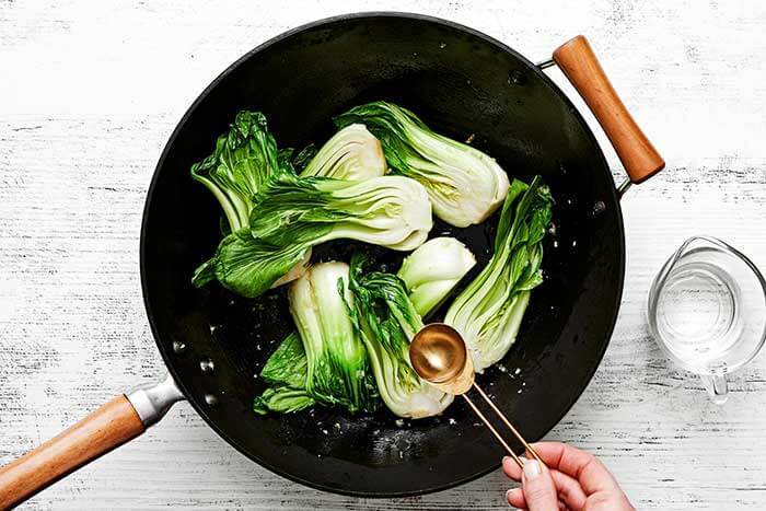 Stir-fry bok choy in a wok.