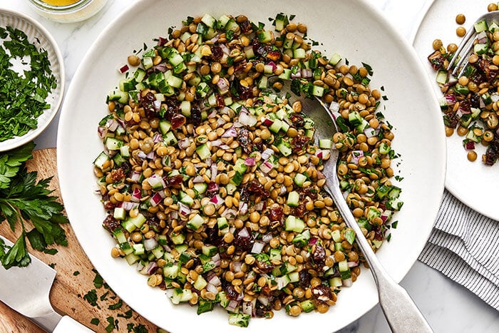 A white bowl of lentil salad with a spoon.
