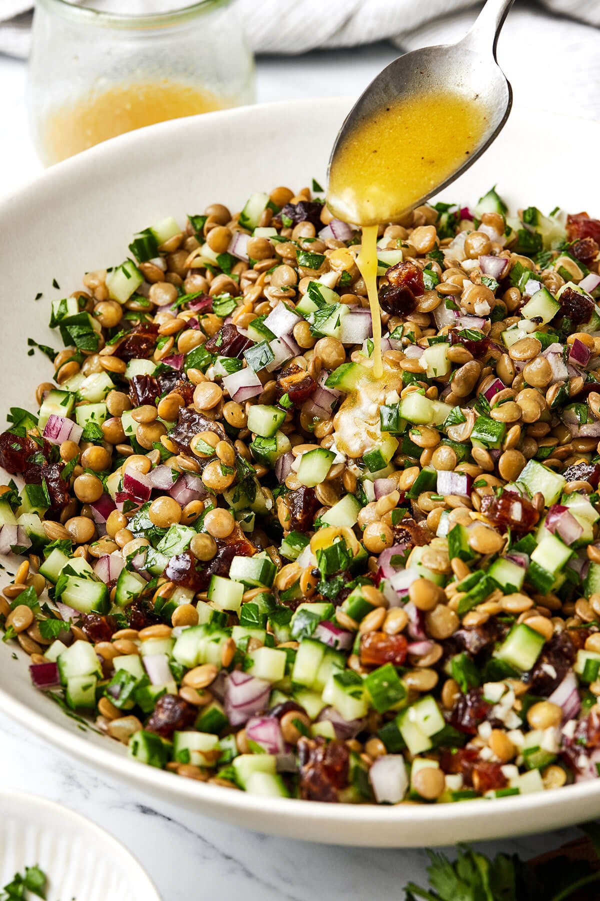 This lentil salad is crisp, fresh, and light with diced cucumber, red onion, dates, fresh herbs, and a bright lemon vinaigrette. Drizzling lemon vinaigrette over lentil salad.