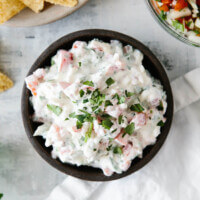 Creamy pico de gallo dip in a black bowl next to chips and salsa.