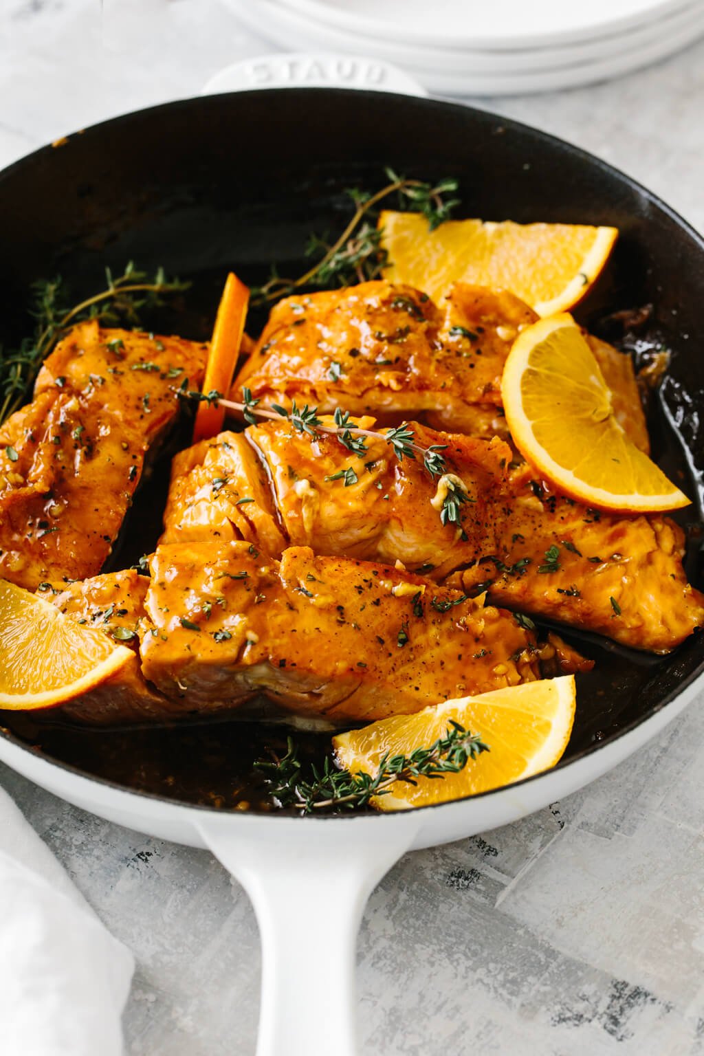 Four salmon filets in a pan with orange slices and thyme on top.