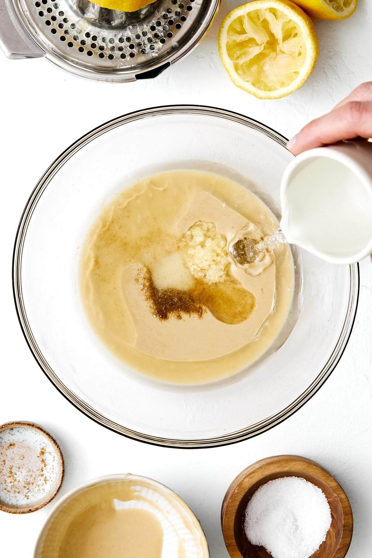 This authentic tahini sauce is easy to make with only a handful of ingredients. Drizzle on falafels, kabobs, roasted vegetables, and more! Making tahini sauce in a bowl.