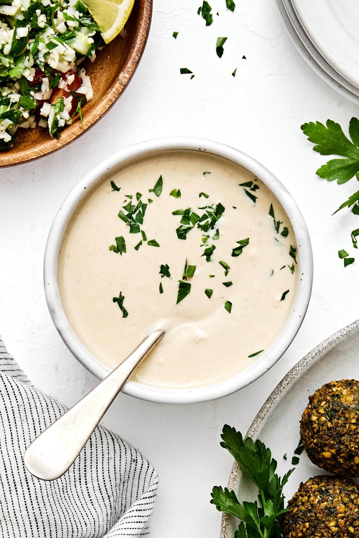 This authentic tahini sauce is easy to make with only a handful of ingredients. Drizzle on falafels, kabobs, roasted vegetables, and more! A bowl of tahini sauce with a spoon.