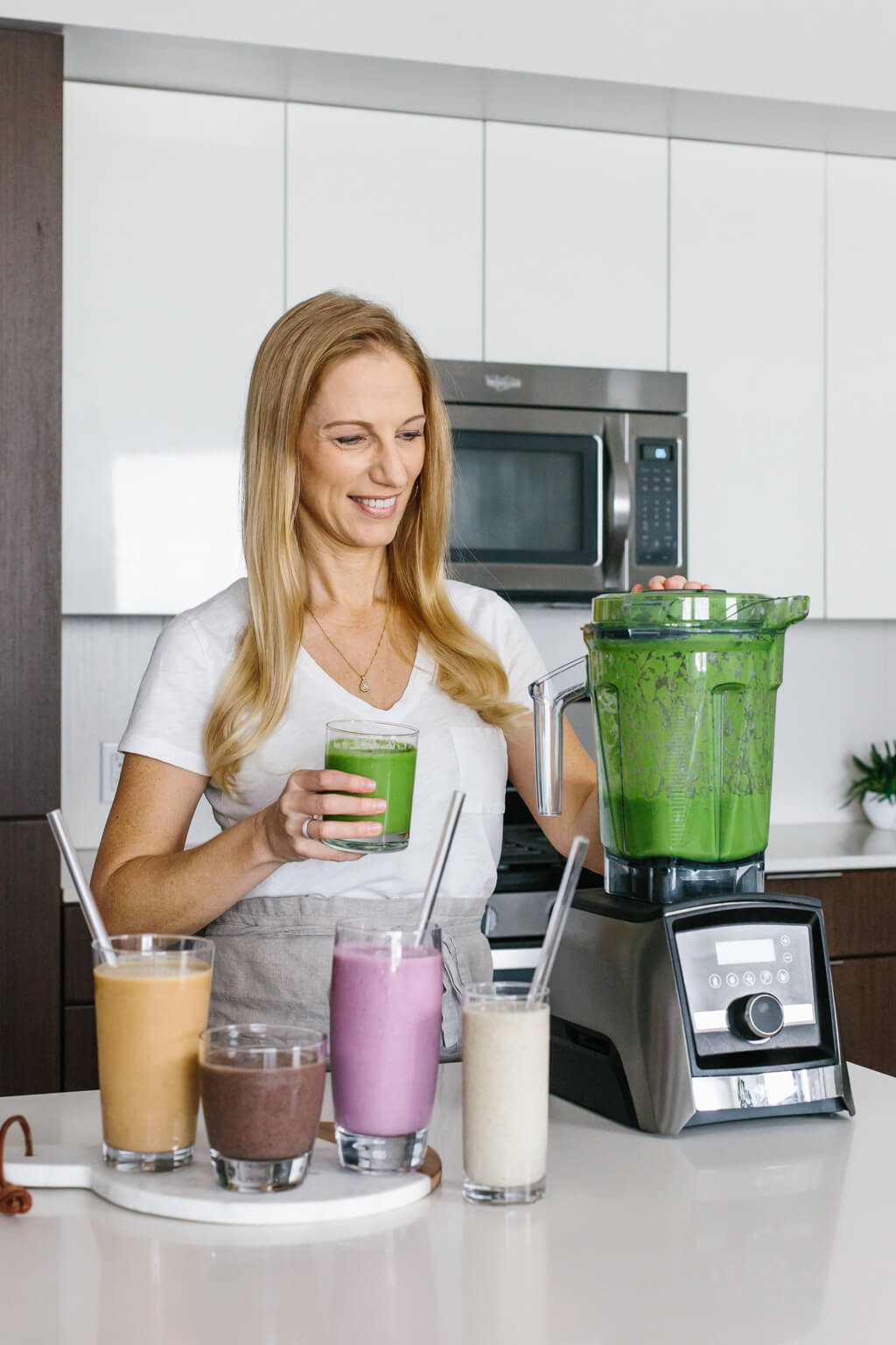 Ready for delicious low sugar smoothies! You're gonna love these 5 healthy smoothie recipes! Lisa Bryan standing next to a Vitamix blender with different colored smoothies.