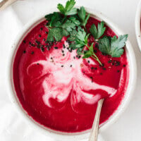 Beet soup in a bowl garnished with coconut cream and parsley.