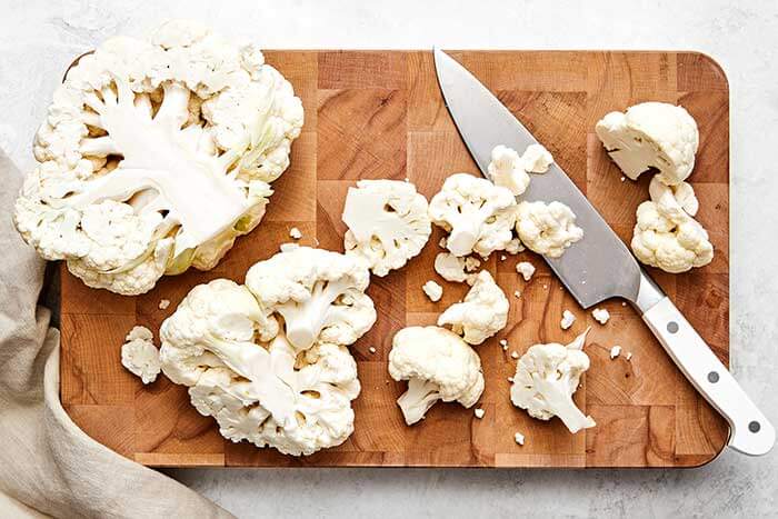 Slicing cauliflower on a wooden board.