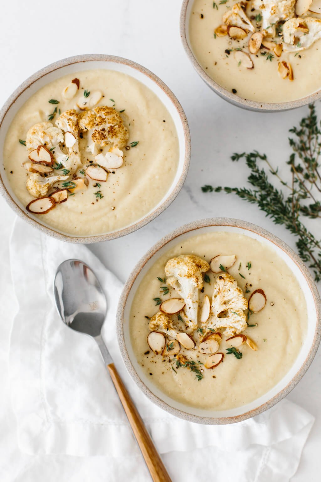 Three bowls of roasted cauliflower soup on a table.