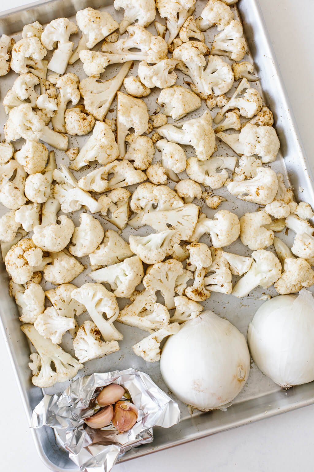 Cauliflower florets on a baking sheet with onion and garlic.