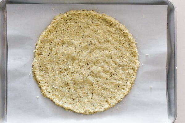 Cauliflower pizza crust formed into a circle on a parchment lined baking tray.