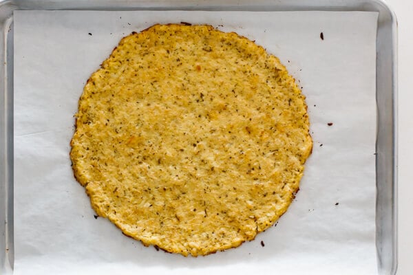 Baked cauliflower pizza crust on a parchment lined baking tray.