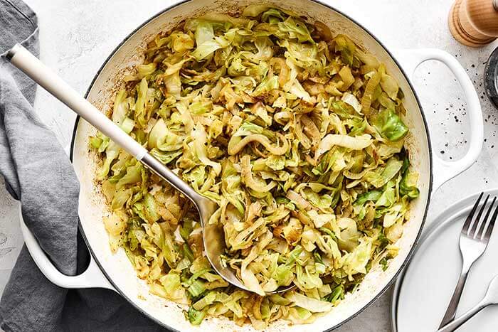 Sauteed cabbage in a white pan with spoon.