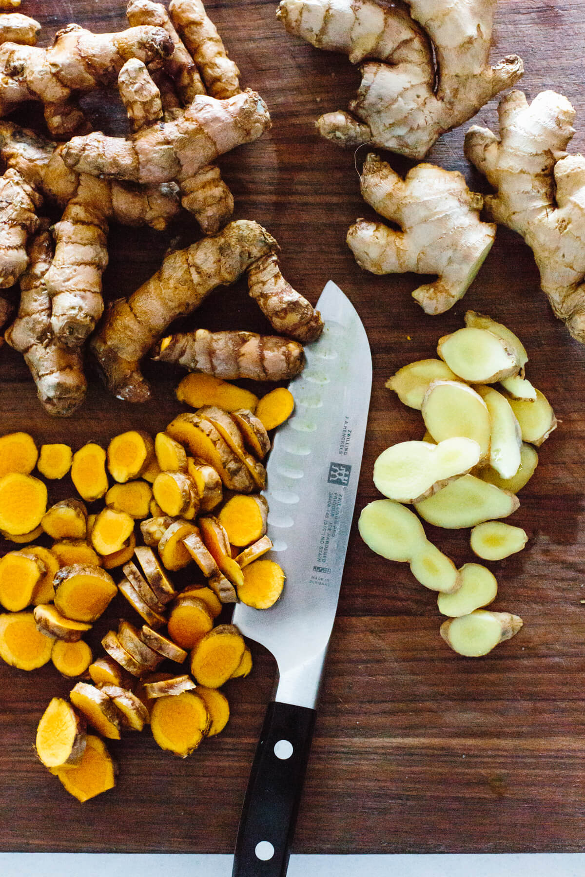 Jamu juice is an Indonesian anti-inflammatory drink that's a blend of fresh turmeric, ginger, lemon, water, and honey. Turmeric and ginger chopped on a cutting board.