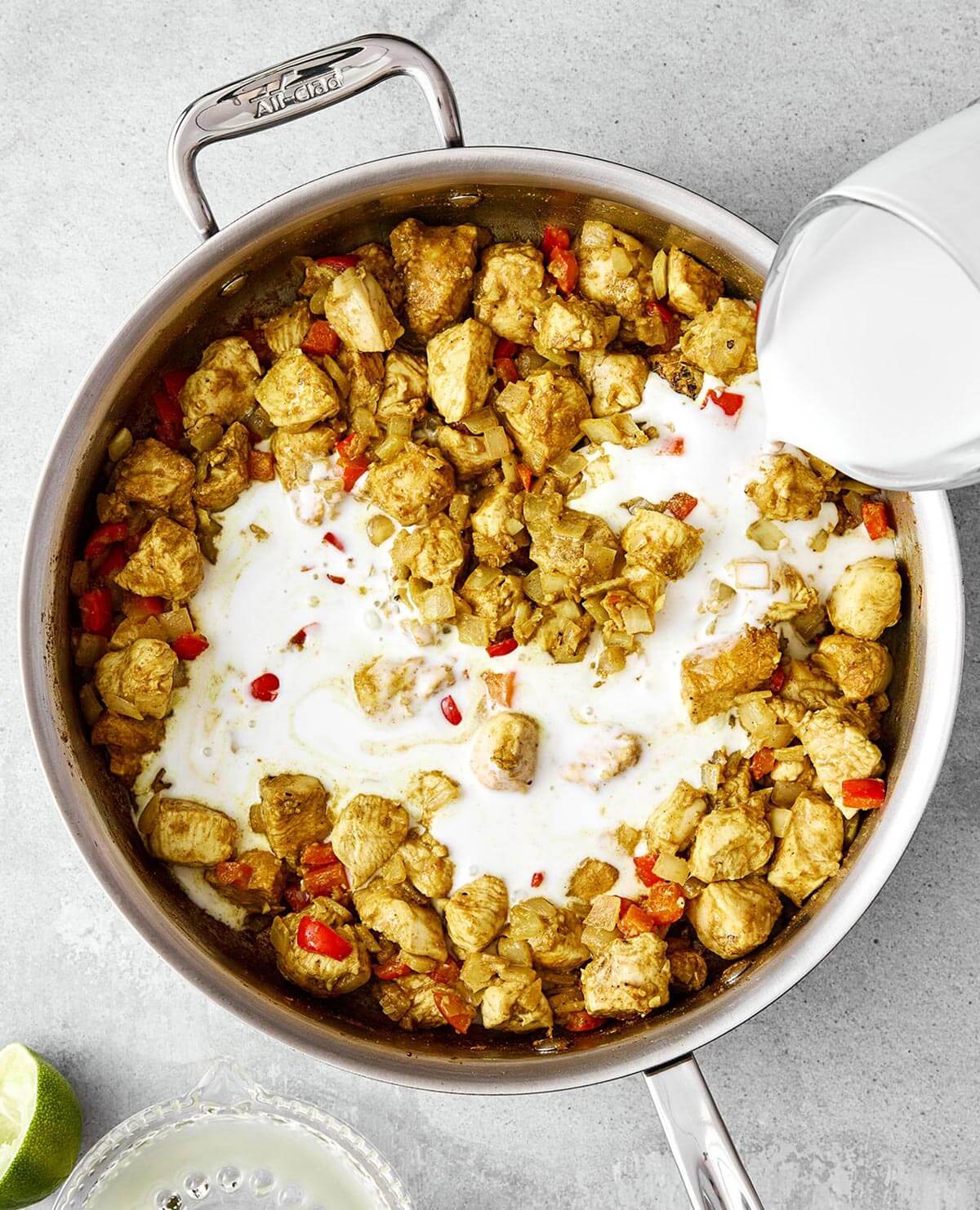 Adding coconut milk into pan with chicken.