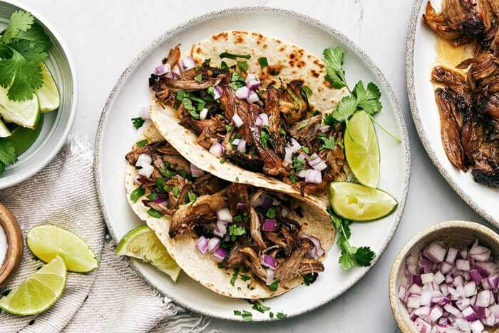 A plate of carnitas tacos with cilantro.