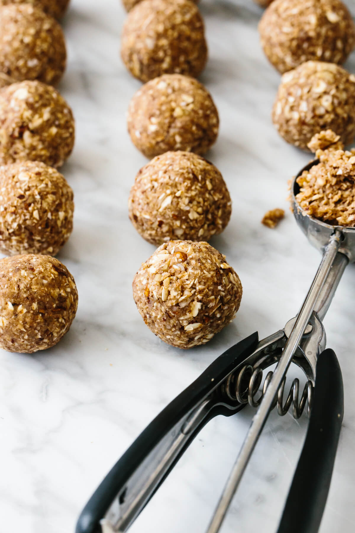 Several energy balls on a counter next to a cookie scoop.