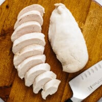 Poached chicken on a cutting board, with one breast sliced up.