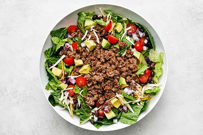Layering a taco salad in a bowl.