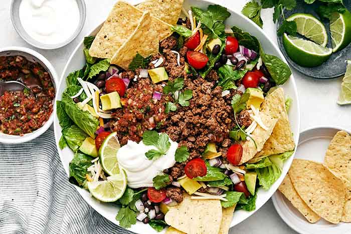A white bowl of taco salad with tortilla chips.