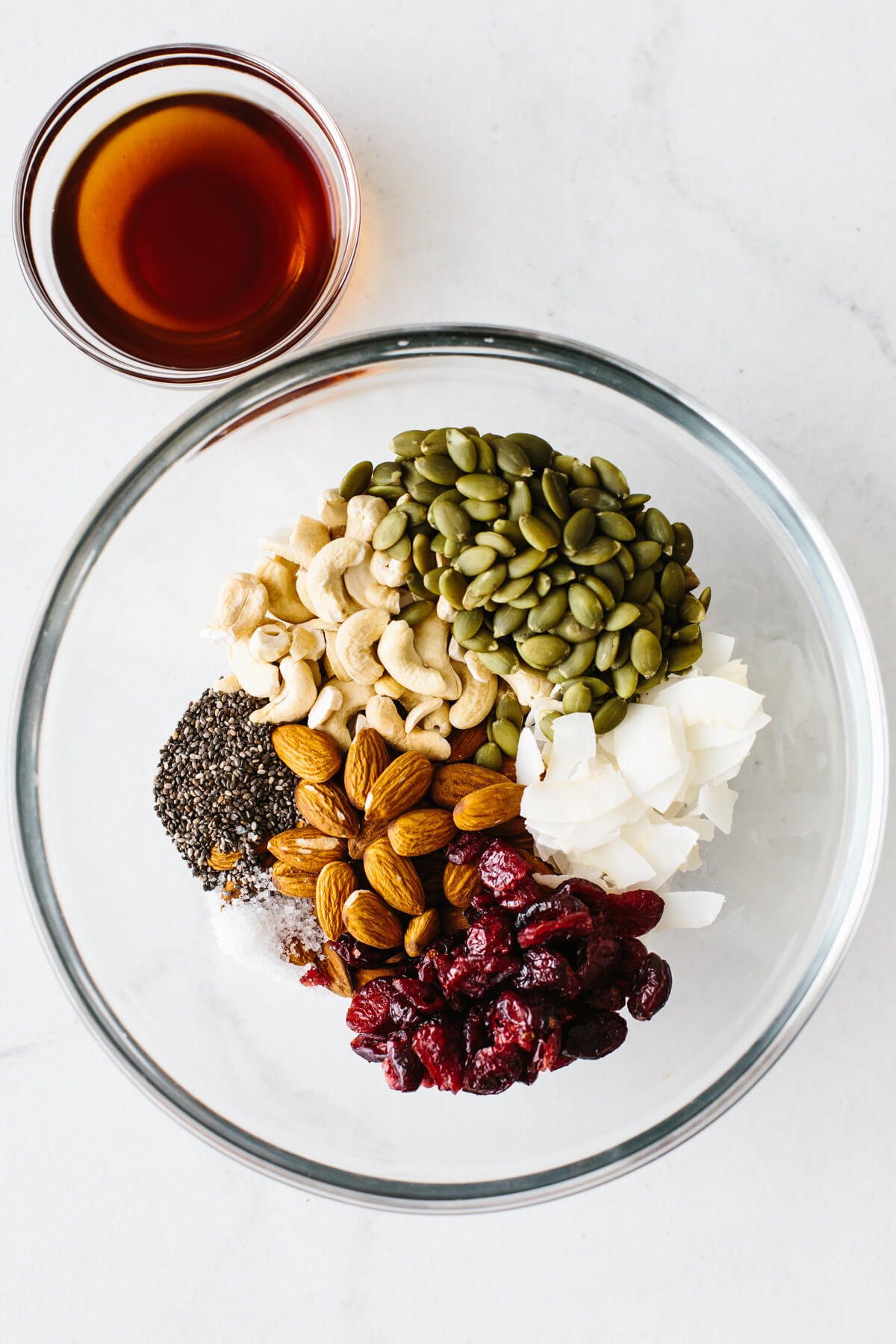 Healthy homemade trail mix granola bars that are gluten-free and paleo friendly! Trail mix granola bar ingredients in a mixing bowl, next to a smaller bowl of maple syrup.