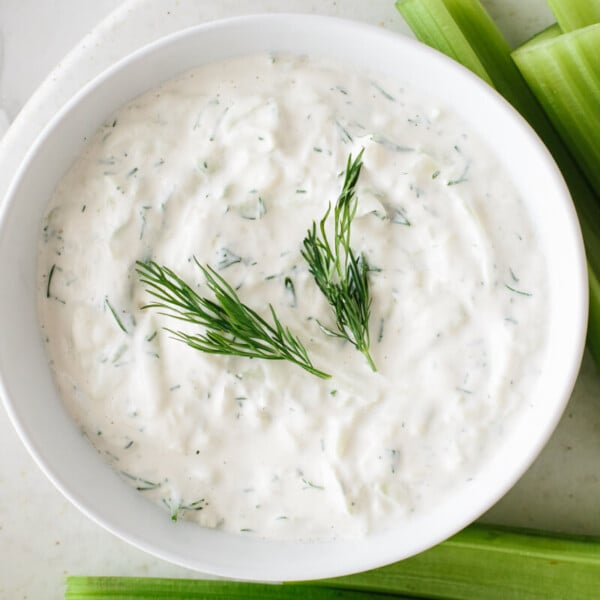 Vegan tzatziki in a bowl garnished with dill and next to pieces of celery.