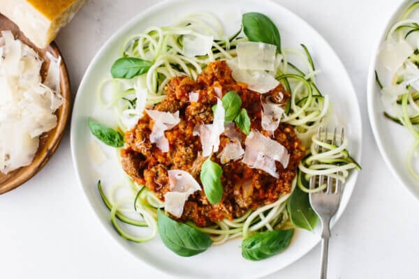 A plate of zucchini noodles topped with bolognese sauce, next to a plate of parmesan.