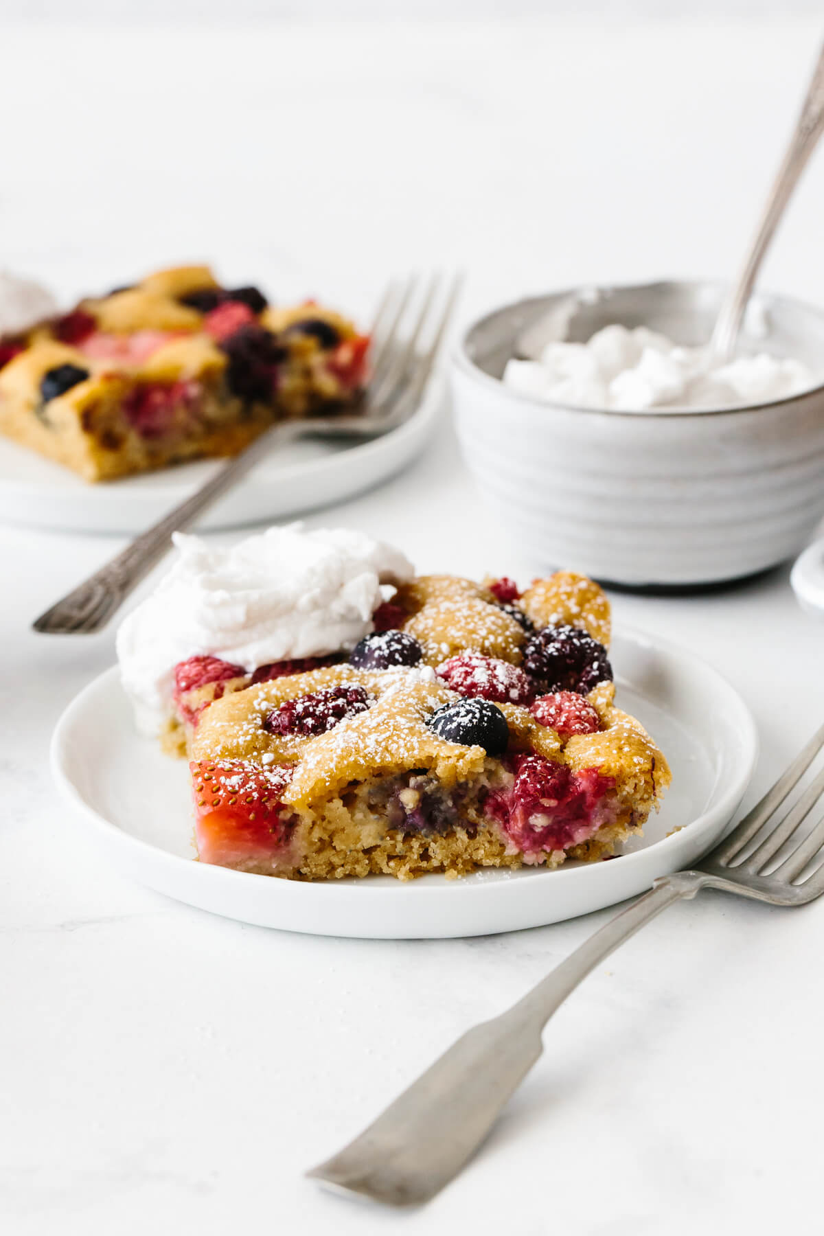 Single serving of berry sheet cake topped with cream and powdered sugar.