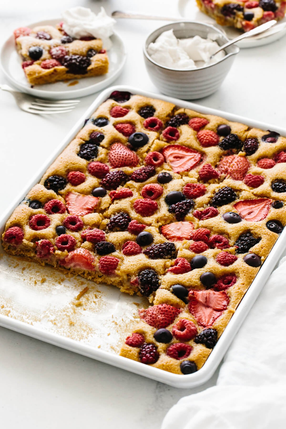 Sheet pan of berry cake with a few servings removed and on plates.