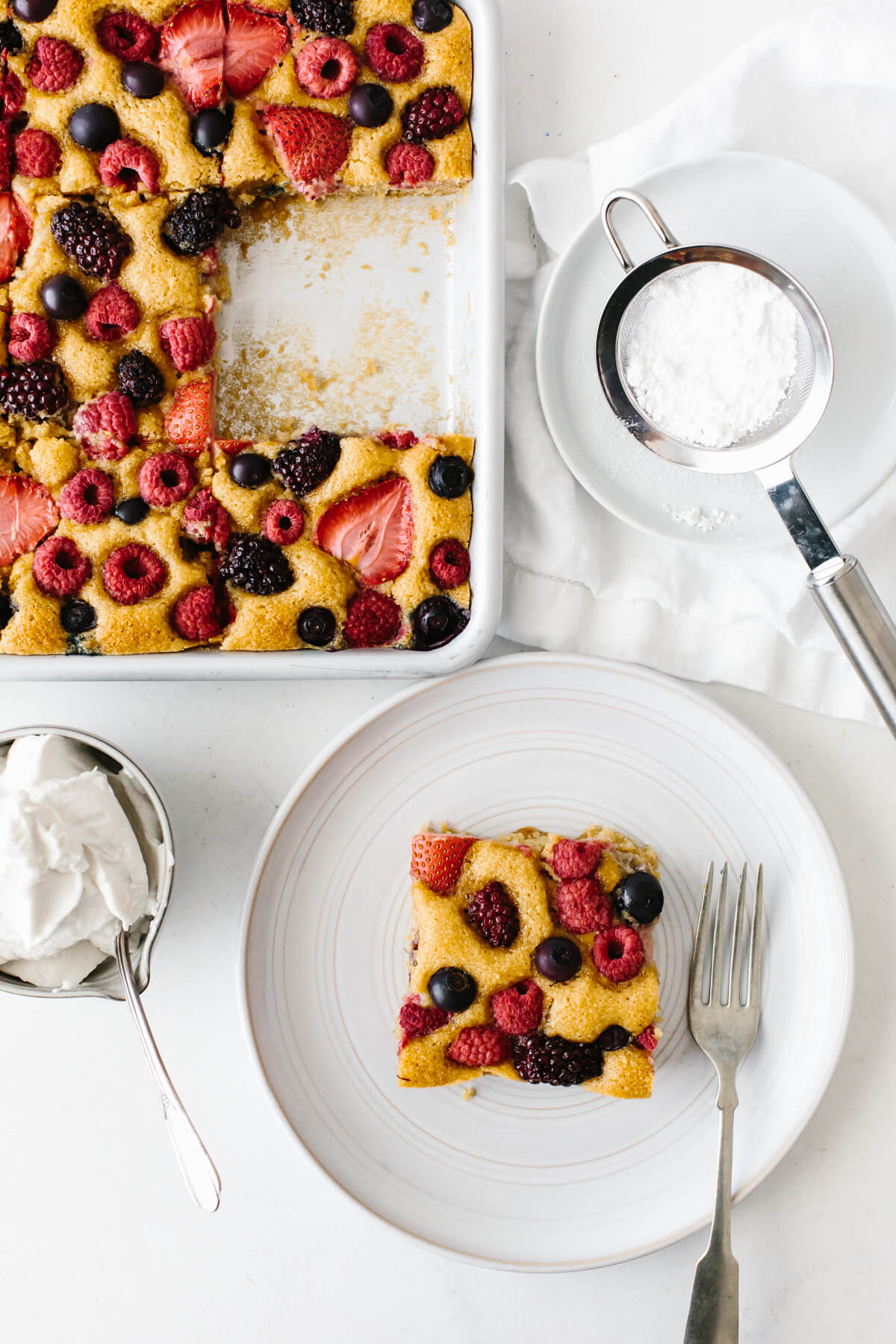 A single serving of berry sheet cake on a plate, next to the pan of cake.