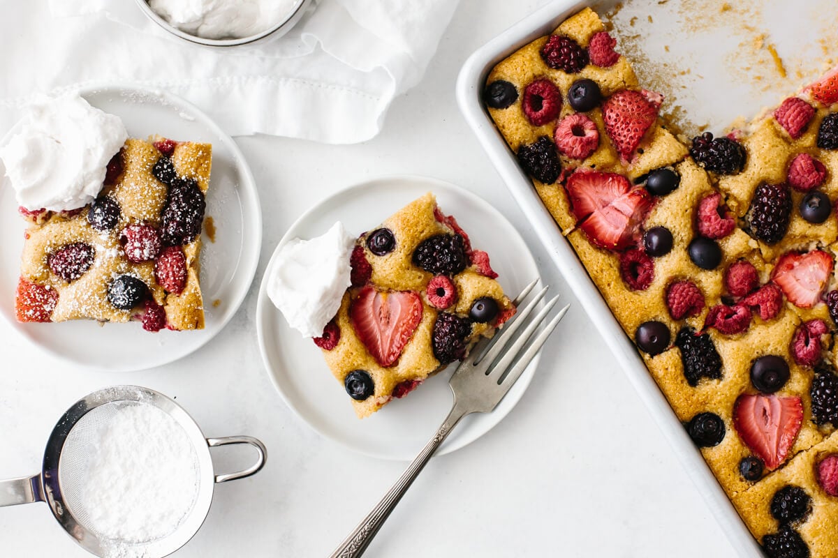 Two servings of berry sheet cake on plates, with cream.