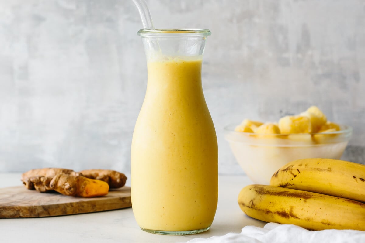 Turmeric smoothie in a glass surrounded by ingredients.