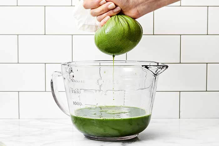 Straining green juice with a nut milk bag.