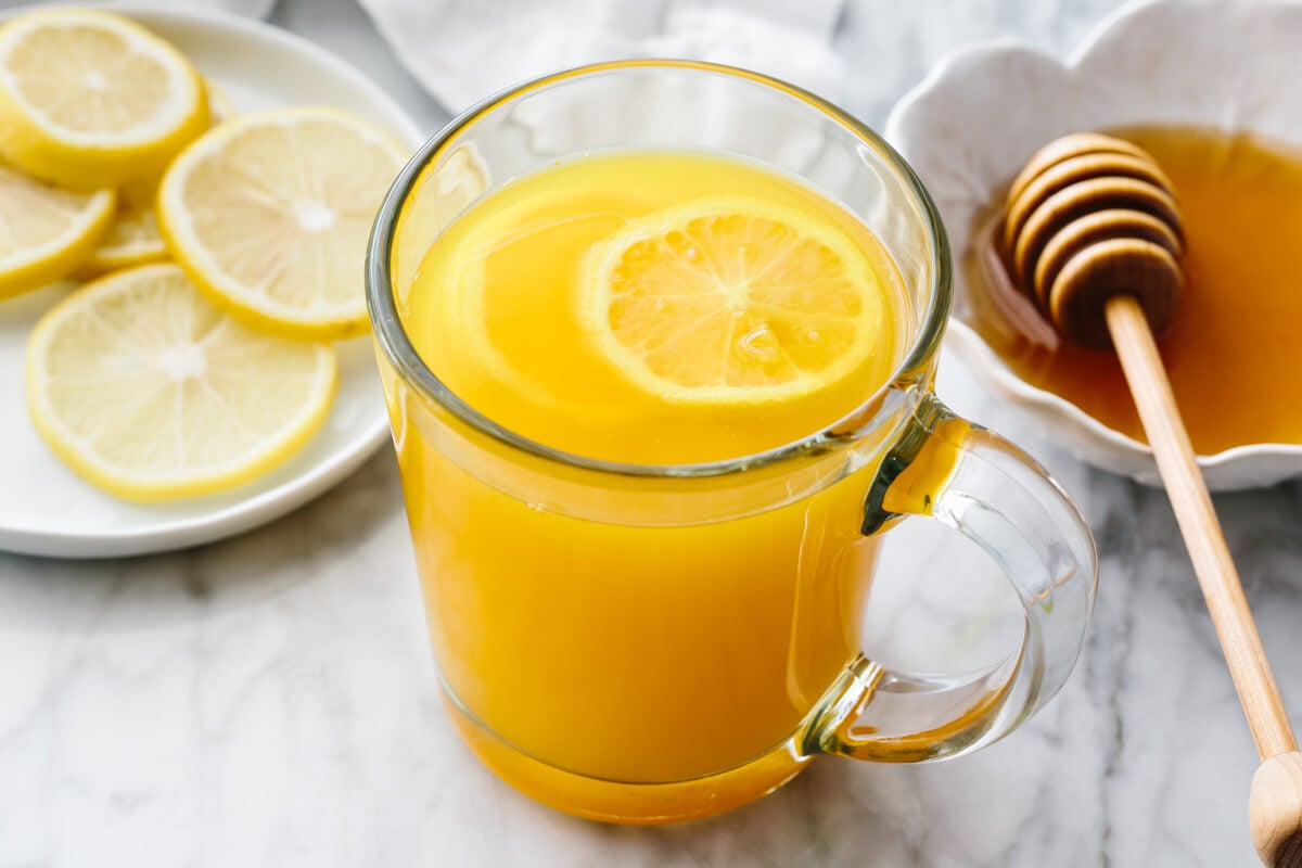 Turmeric tea is a blend of ground turmeric, lemon juice, and honey that's anti-inflammatory and immune-boosting. Turmeric tea in a glass with honey and lemon slices in the background.