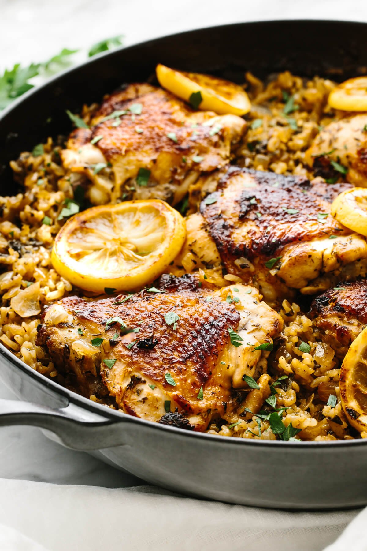 Chicken and rice is an easy, one pan recipe that shines with bright Mediterranean flavors and juicy chicken thighs! Cooked chicken sitting on top of fluffy rice in a pan.