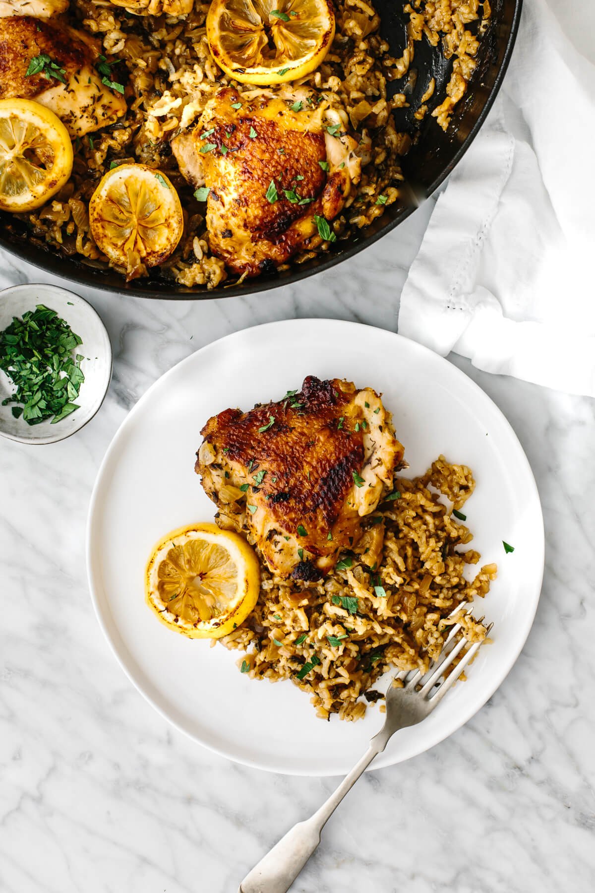 Chicken and rice is an easy, one pan recipe that shines with bright Mediterranean flavors and juicy chicken thighs! A plate with chicken and rice, next to the pan.