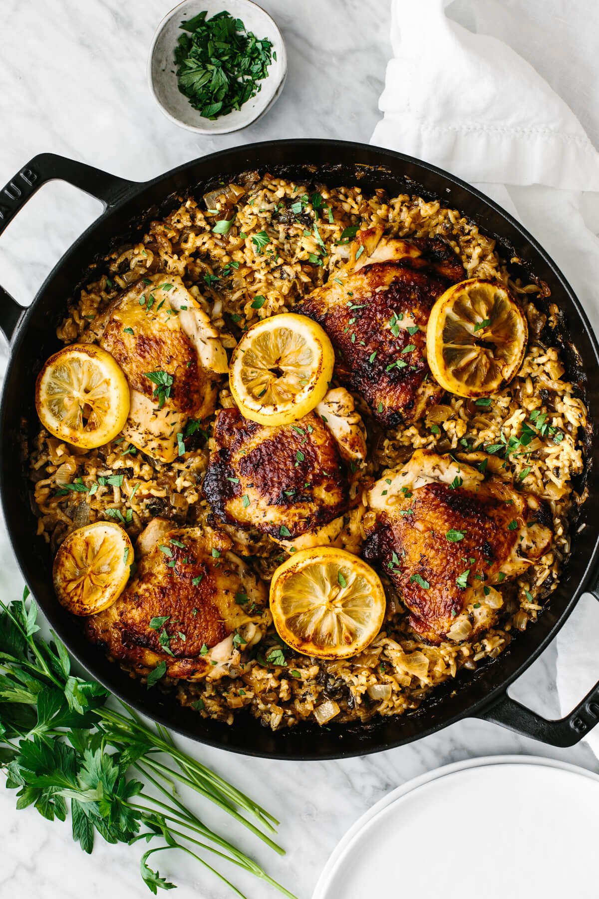 Chicken and rice is an easy, one pan recipe that shines with bright Mediterranean flavors and juicy chicken thighs! Chicken and rice in one pan garnished with lemon slices and parsley.