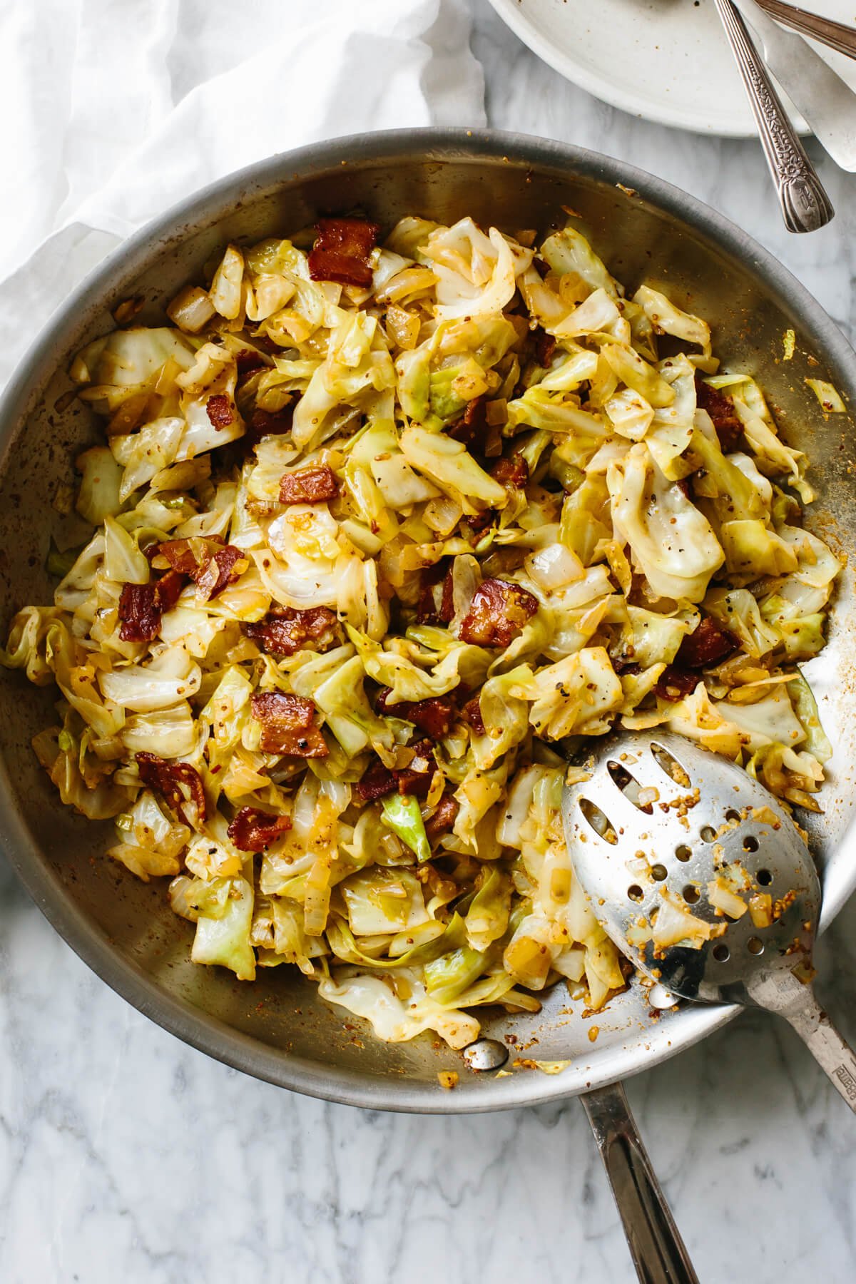 Fried cabbage in a pan with a serving spoon on a table.