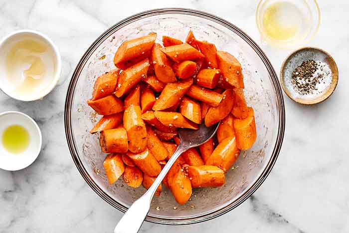 Tossing carrots in a bowl with spices and honey.